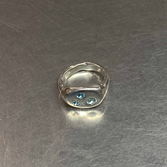 Silver ring with blue topaz gemstones on a metallic surface