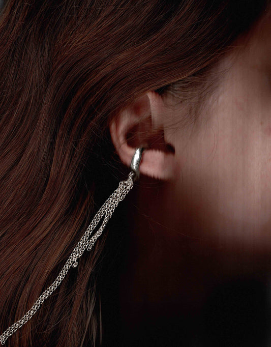Close-up of a silver hoop earring with a chain detail worn by a person.