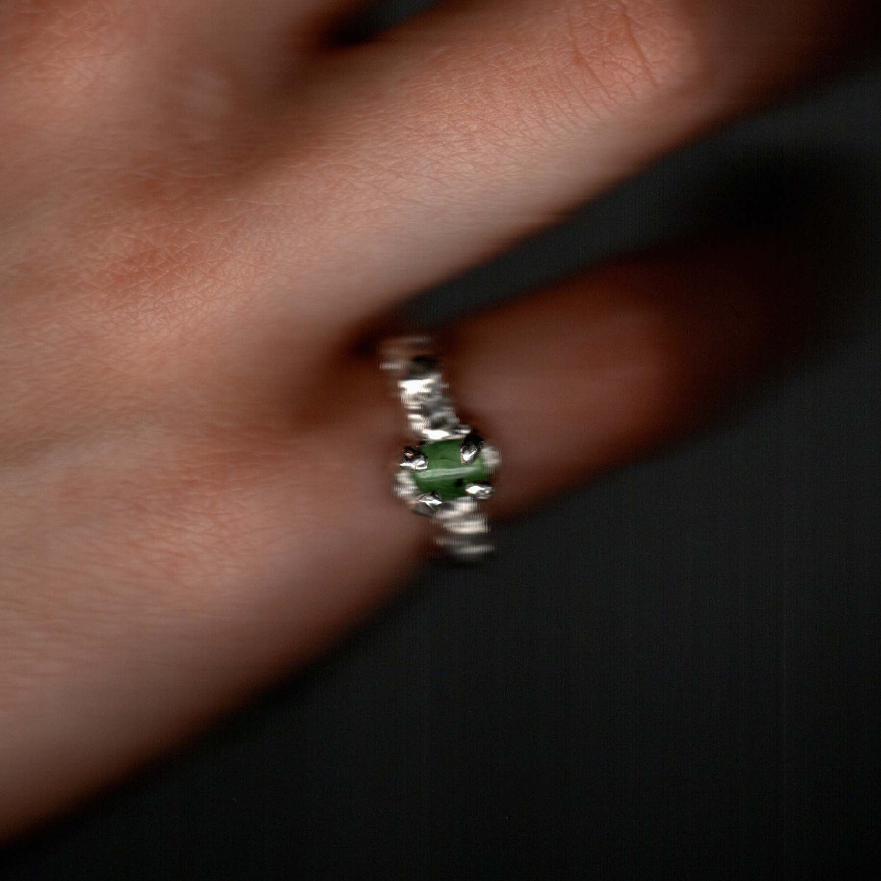 Silver ring with an emerald gemstone on a finger.  Daras Space
