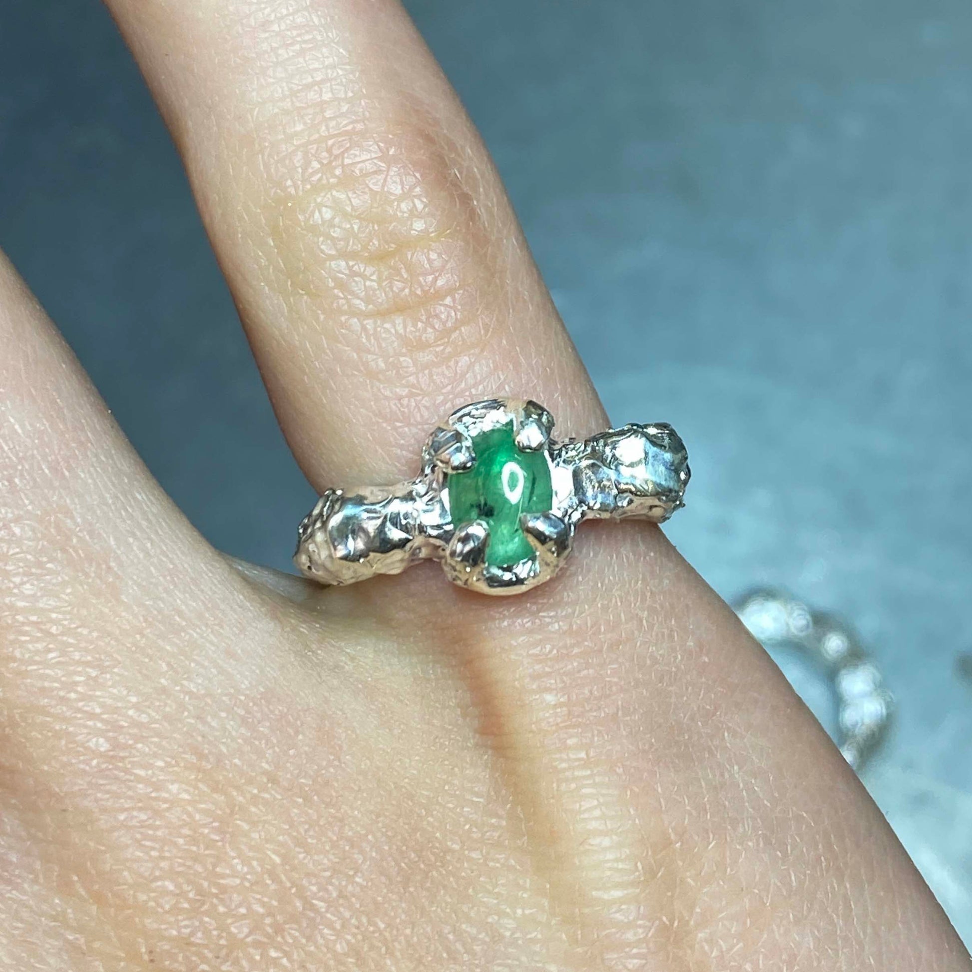 Silver ring with an emerald gemstone on a finger.  Daras Space