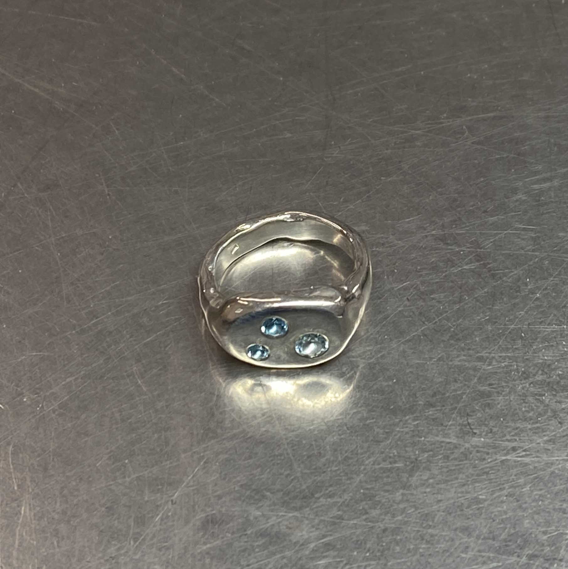 Silver ring with blue topaz gemstones on a metallic surface