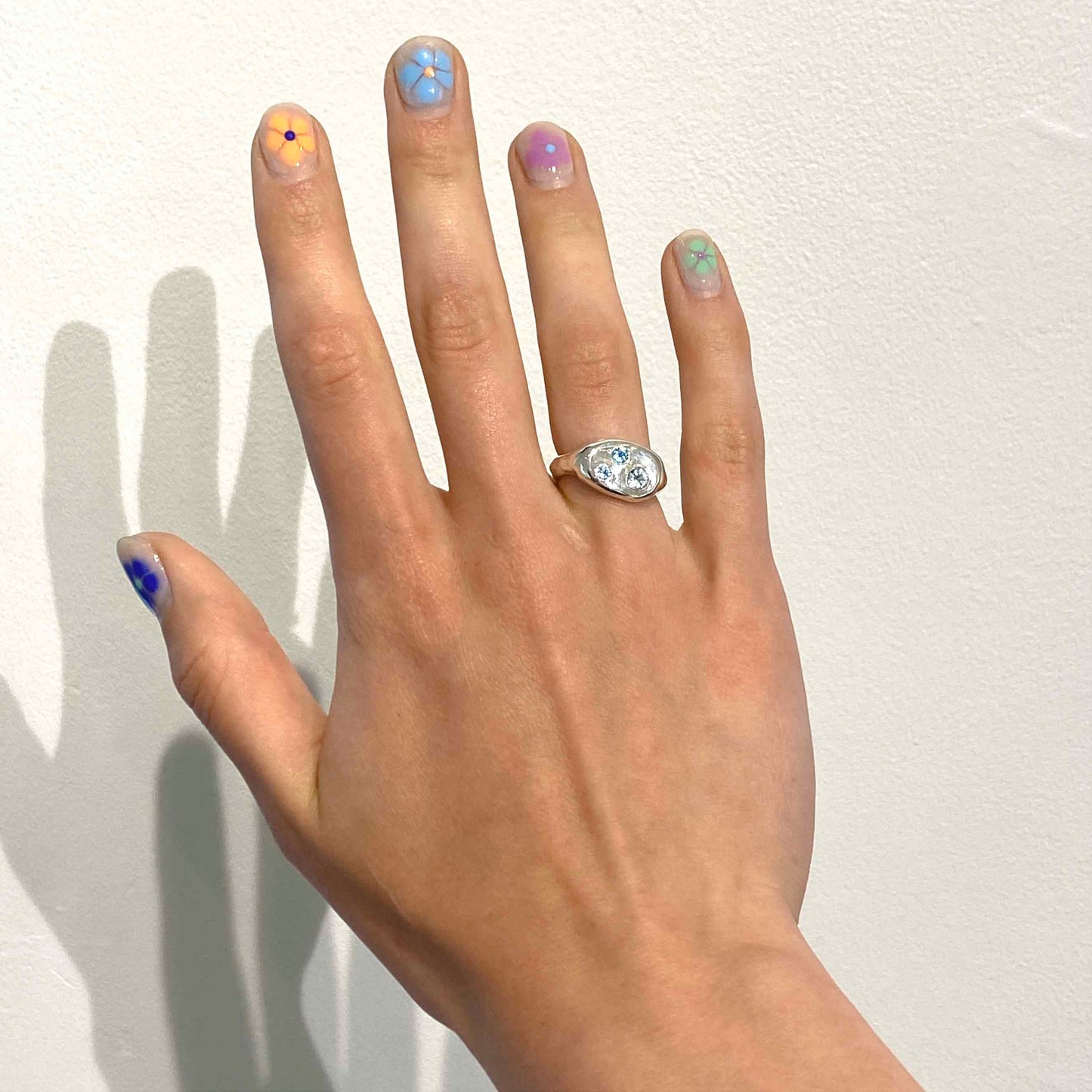 Silver ring with blue topaz gemstones on a finger against a white background. 