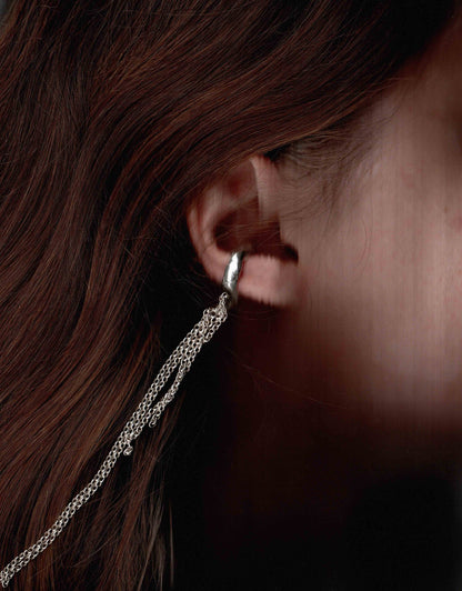 Close-up of a silver hoop earring with a chain detail worn by a person.