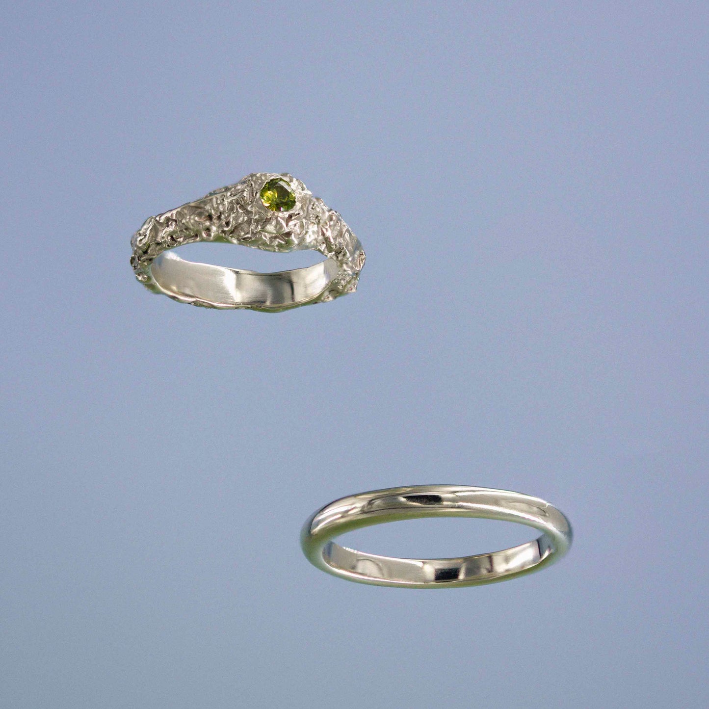 Two old rings with a green sapphire on a light blue background
